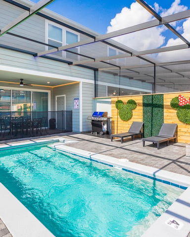 Covered pool deck with turquoise swimming pool, lounge chairs, decorative wall with topiary, and modern house with glass doors